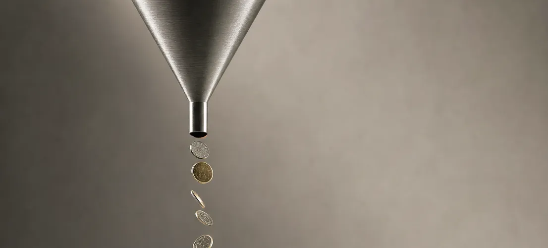 Monedas cayendo por un embudo hacia una superficie vacía, representando presupuesto de ads desperdiciado