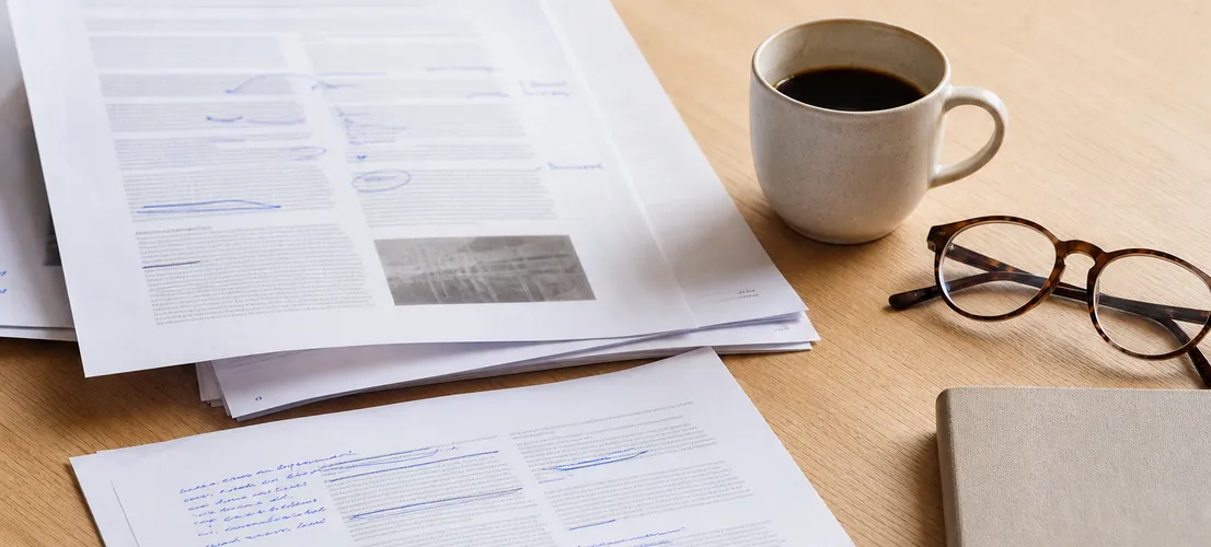 Documentos de contenido revisados a mano sobre un escritorio, representando el ajuste de la voz de marca en servicios profesionales